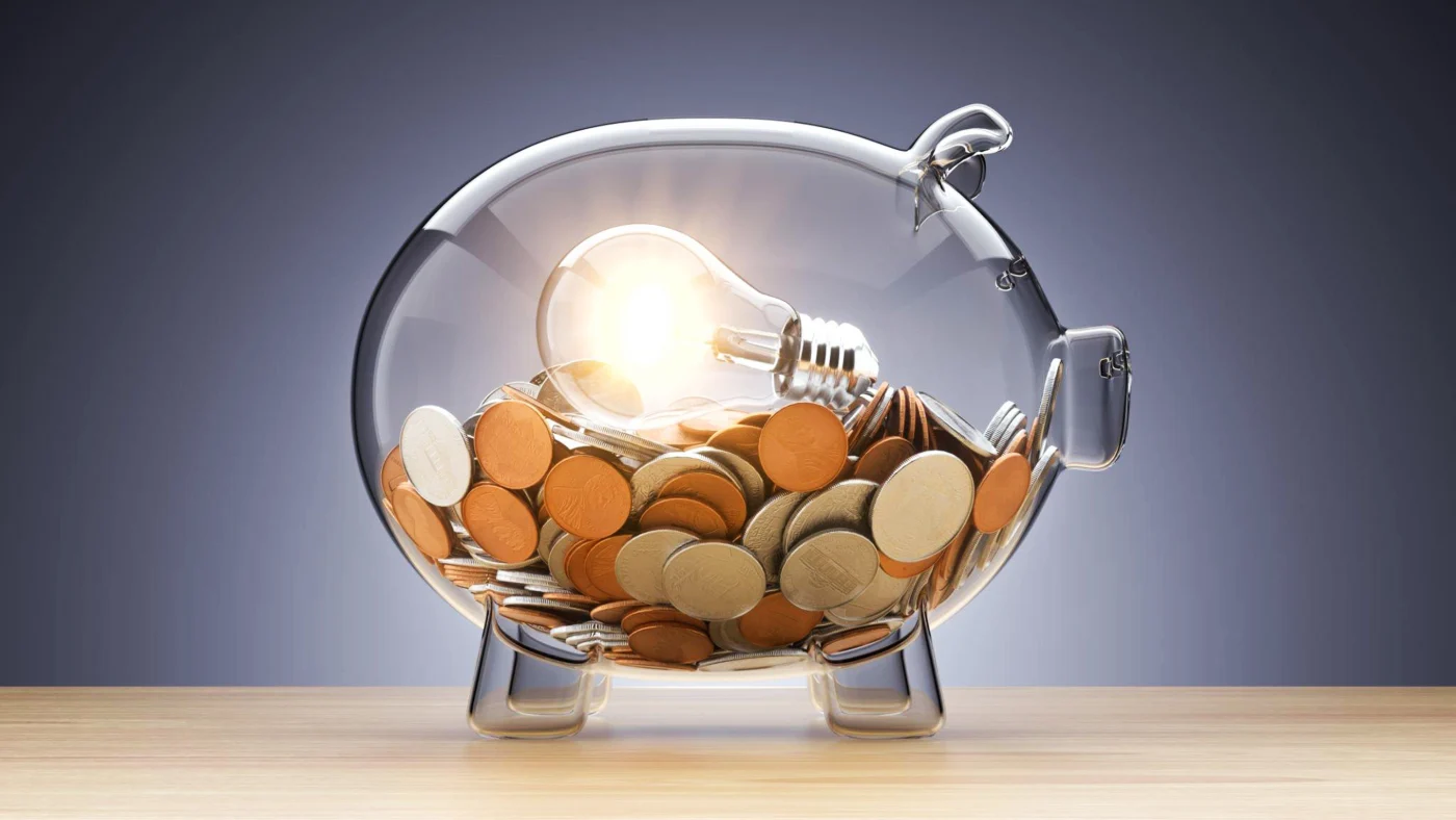 Roofing Financing - San Antonio - Lynx Roofing A clear glass piggy bank filled with coins and an illuminated lightbulb