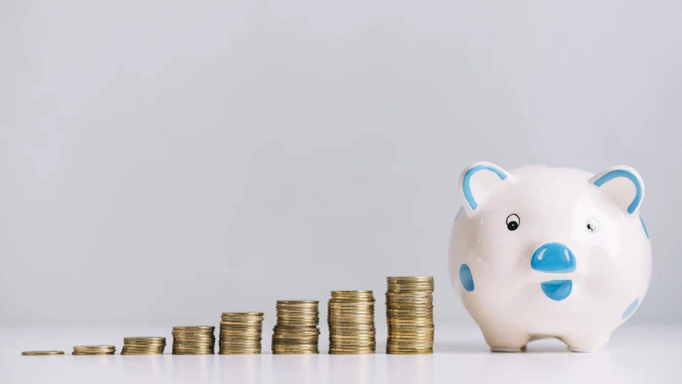Stacks of coins increase in size as they move toward a blue and white piggy bank