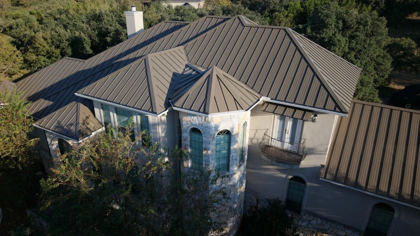 Top Tier Metal Roofing Services | North San Antonio, TX | Lynx Roofing, LLC Aerial view of a lakeside home with a red metal roof surrounded by neighboring houses.