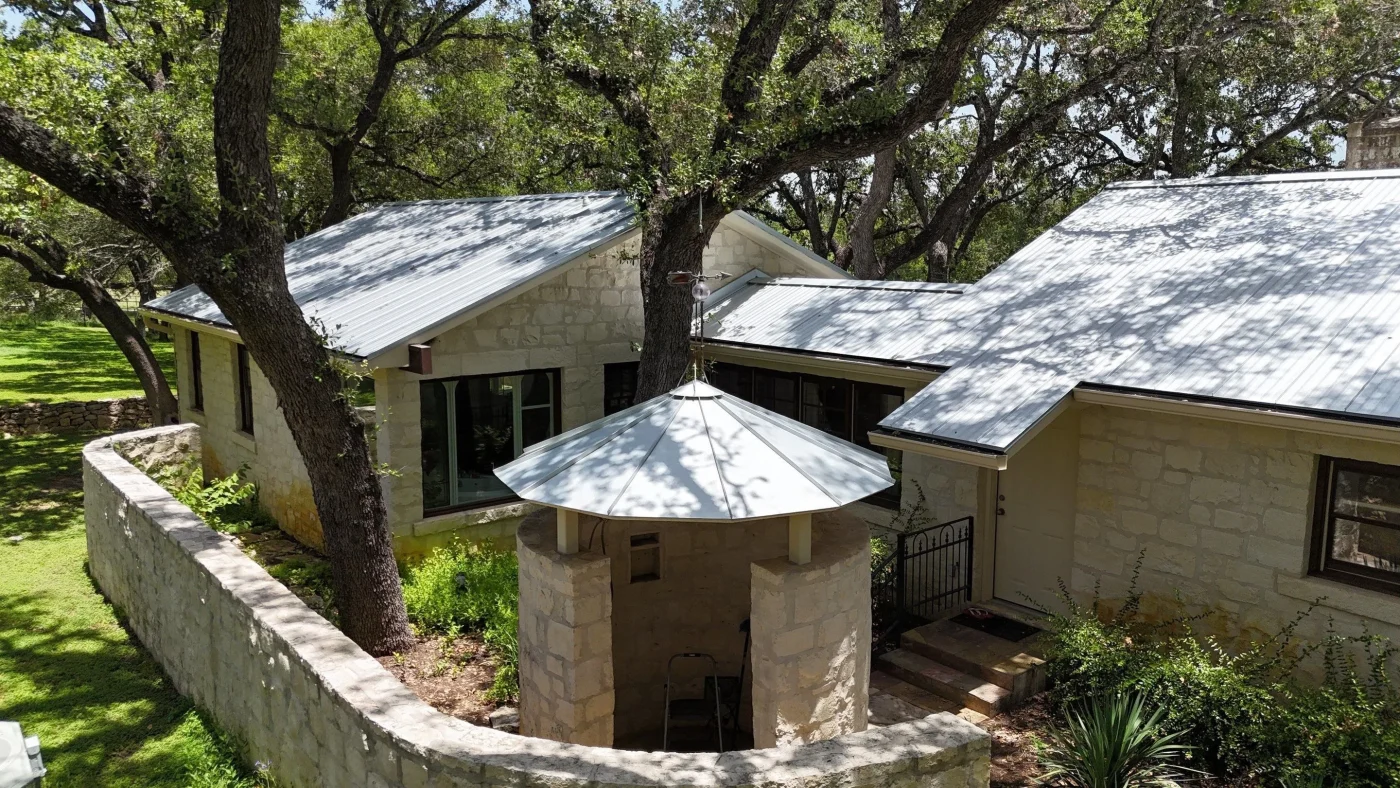 Stone home surrounded by mature trees with a bright silver metal roof.